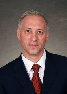 A man in suit and tie standing up against a wall.